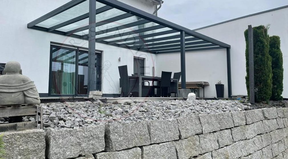 Angebaute Terrassenüberdachung aus anthrazitfarbenem Aluminium mit Glasdach über einer Terrasse mit Sitzgruppe